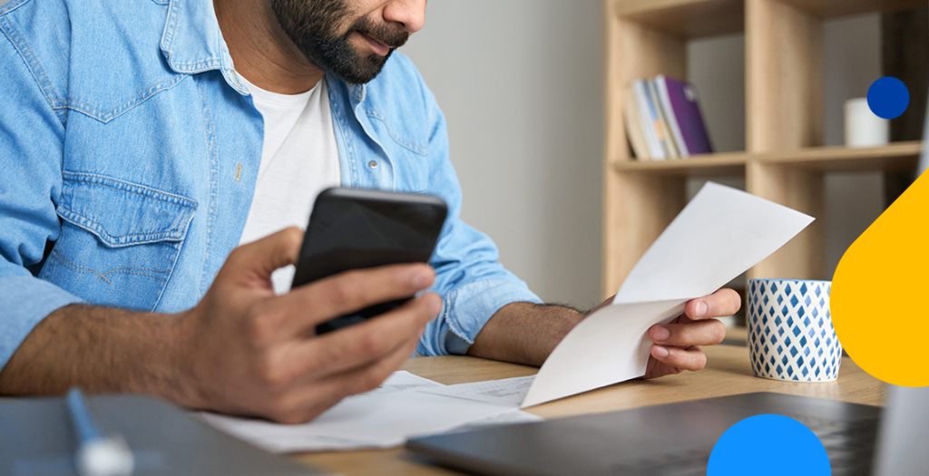 um homem segurando o celular e uma nota fiscal mei nas mãos